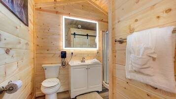 A wooden cabin bathroom with a toilet, sink, and mirror.