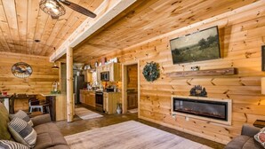 A log cabin interior with a fireplace, wooden walls, a kitchen area, and a dining space.