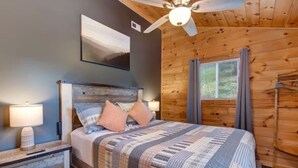 A bedroom with a bed, a ceiling fan, a window with curtains, and a wall-mounted picture.