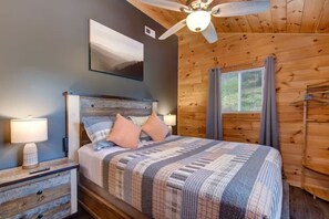 Un dormitorio con cama, ventilador de techo, ventana con cortinas e imagen colgada en la pared.