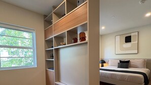 A bedroom with a bed, a large wardrobe, two black stools, and a window with a view of greenery. - 101 Wave Miami Beach (Miami Beach)
