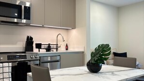 A modern kitchen with stainless steel appliances, a dining table with chairs, and a potted plant. - 101 Wave Miami Beach (Miami Beach)