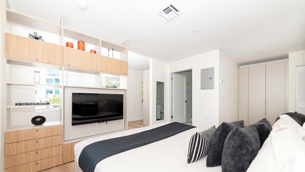A modern bedroom with a bed, TV, built-in wardrobe, and a small desk area. - 101 Wave Miami Beach (Miami Beach)
