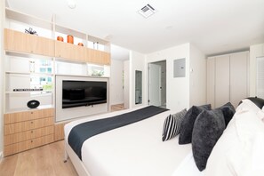 A modern bedroom with a bed, TV, built-in wardrobe, and a small desk area. - 101 Wave Miami Beach (Miami Beach)