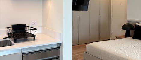 A modern bedroom with a bed, a TV mounted on the wall, and a separate kitchenette area with a dishwasher.