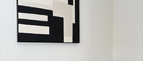 A modern bedroom with a large abstract painting, a bed with multiple pillows, and a nightstand with a lamp.