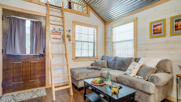 A cozy living room with a sofa, a coffee table, a wooden ladder, and a door with curtains. - Skyview Ranch Family Cabin (Bluff Dale)