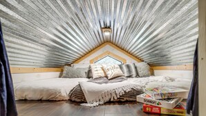 A cozy attic bedroom with a sloped ceiling, a bed with a blanket and pillows, and a box of board games on the floor. - Skyview Ranch Family Cabin (Bluff Dale)