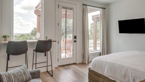A bedroom with a bed, two chairs, a TV, and a window with curtains.