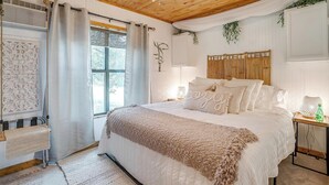Une chambre avec un plafond en bois, un lit avec une literie blanche, une table de chevet avec une lampe et une fenêtre avec des rideaux.