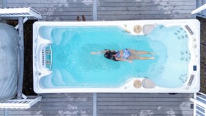 Un jacuzzi rectangulaire dans lequel une personne nage, entouré d’une terrasse en bois.