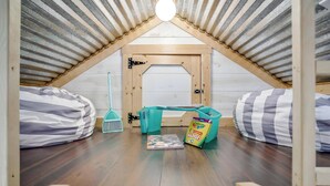 Une petite pièce mansardée avec un plafond en pente, une porte en bois, deux fauteuils en forme de sac, une petite table et une boîte de crayons de couleur Crayola.