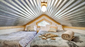 Une chambre mansardée chaleureuse, avec un plafond en pente, un puits de lumière, deux lits avec des oreillers et une petite table sur laquelle sont posés des blocs de bois.