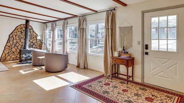 A room with a stone fireplace, large windows, a door with a geometric design, and a patterned rug. - Private Boat Dock at Waterfront Lake Mitchell Home (Cadillac)