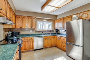 A kitchen with wooden cabinets, a stainless steel refrigerator, a microwave, and a dishwasher. - Private Boat Dock at Waterfront Lake Mitchell Home (Cadillac)