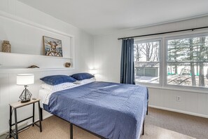 Ein Schlafzimmer mit Bett, Nachttisch, Lampe, einem gerahmten Bild und einem Fenster mit Vorhängen.