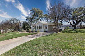 A single-story house with a front yard, a driveway, and a large tree to the right.