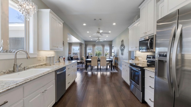 A modern kitchen with white cabinetry, stainless steel appliances, a granite countertop, and a dining area with a chandelier. - Beloved Haus - Hot-Tub, 4-Min to Main Street! (Fredericksburg)