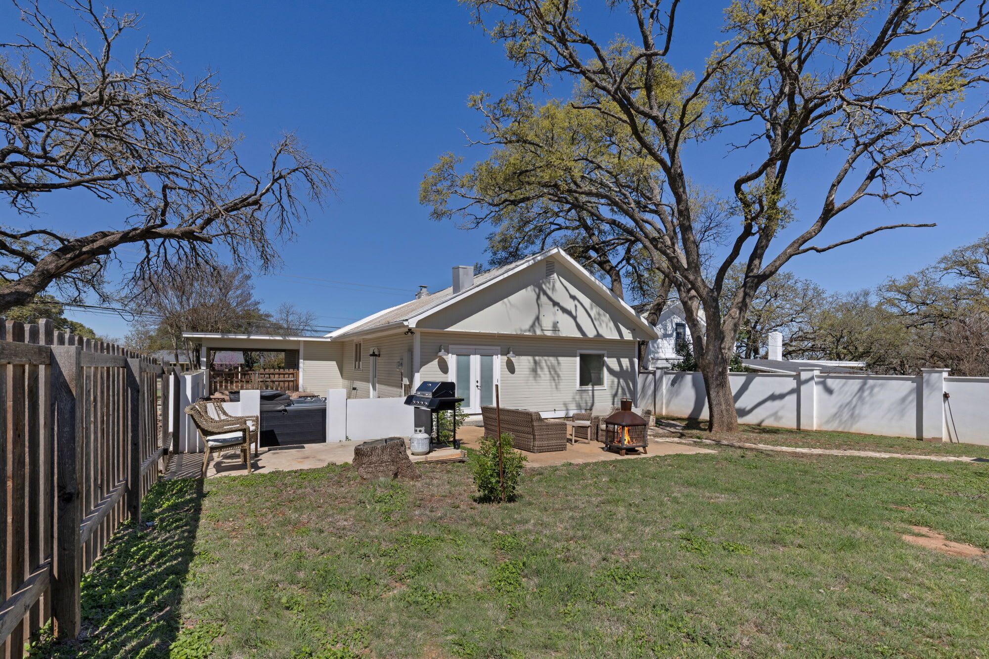 A house with a fenced backyard, a barbecue area, and a small tree.