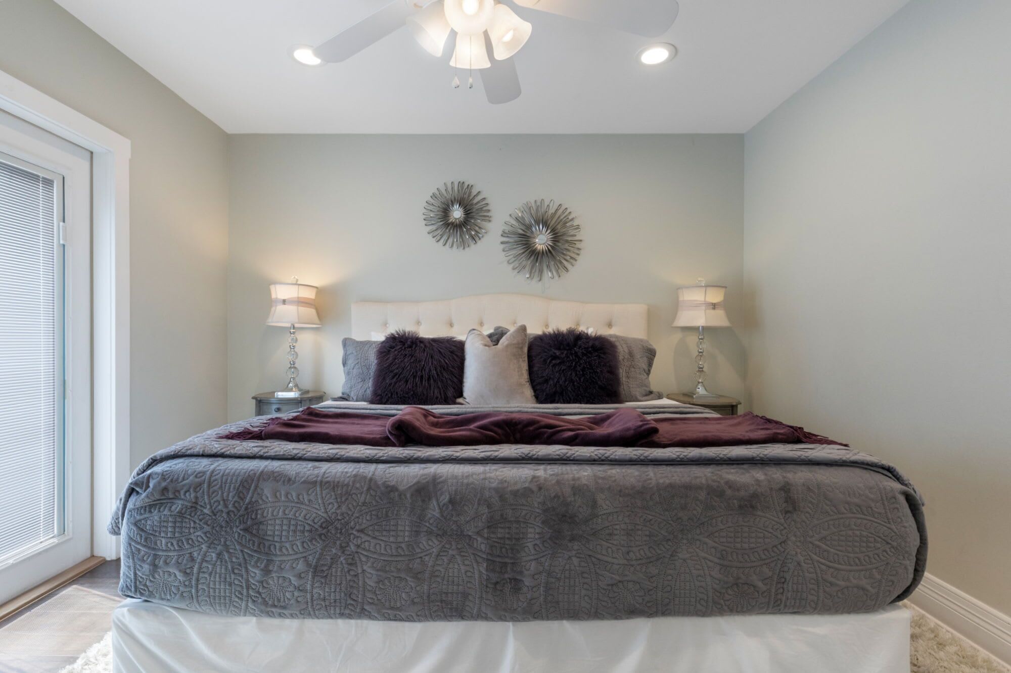 A bedroom with a bed, two wall sconces, a ceiling fan, and two wall decorations.