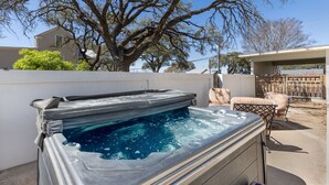 A hot tub with a wooden deck, a large tree, and a covered patio area. - Beloved Haus - Hot-Tub, 4-Min to Main Street! (Fredericksburg)