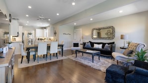 A spacious living room with a dining area, a black sofa, a white armchair, and a large mirror. - Beloved Haus - Hot-Tub, 4-Min to Main Street! (Fredericksburg)