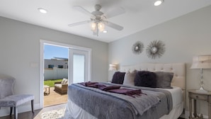 A bedroom with a bed, a ceiling fan, a nightstand, a lamp, and a view of the outdoors. - Beloved Haus - Hot-Tub, 4-Min to Main Street! (Fredericksburg)