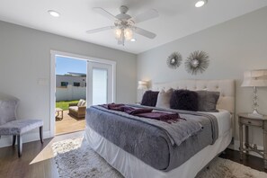 A bedroom with a bed, a ceiling fan, a nightstand, a lamp, and a view of the outdoors.