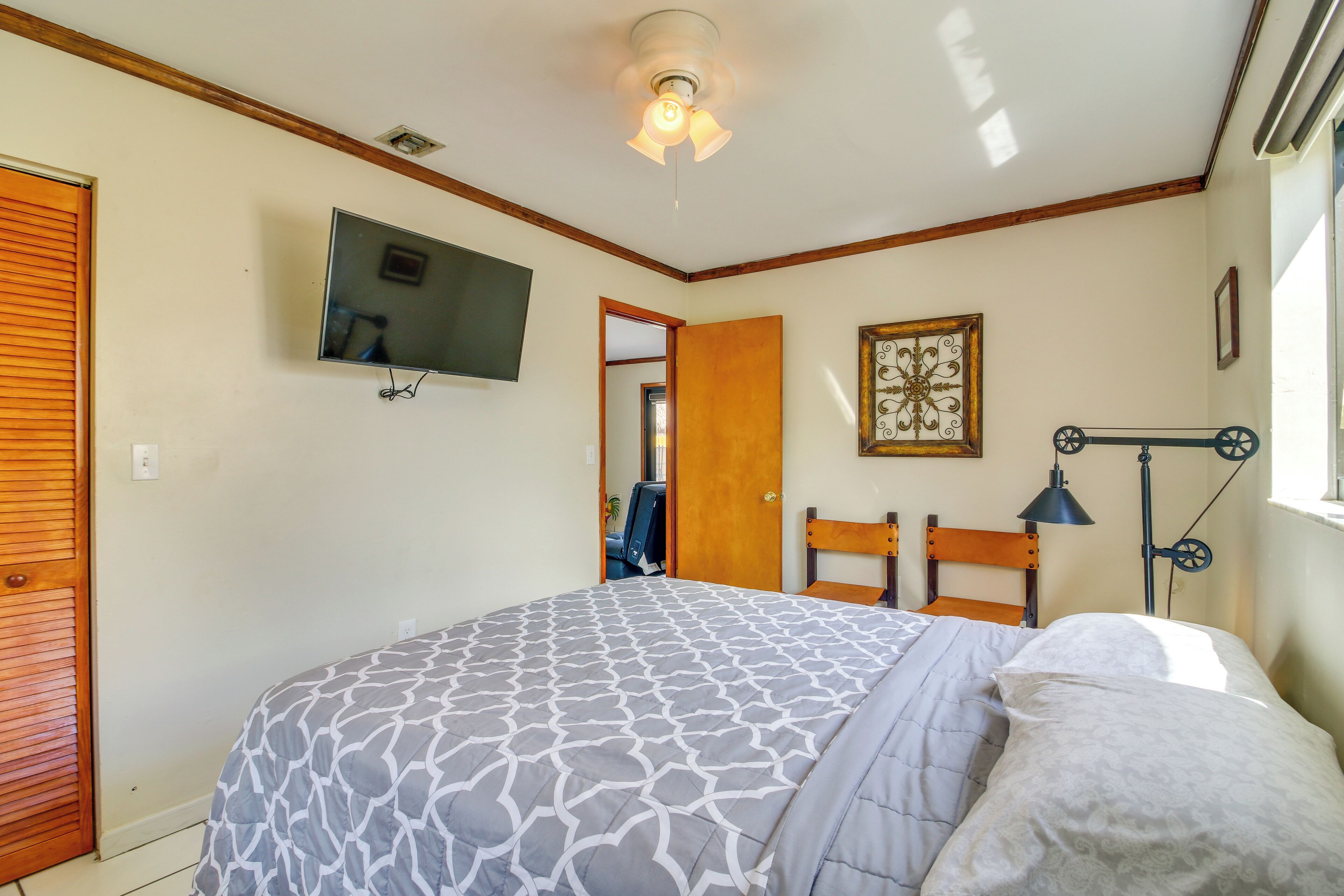 A bedroom with a bed, a ceiling fan, a TV, a wooden door, and a framed picture on the wall.