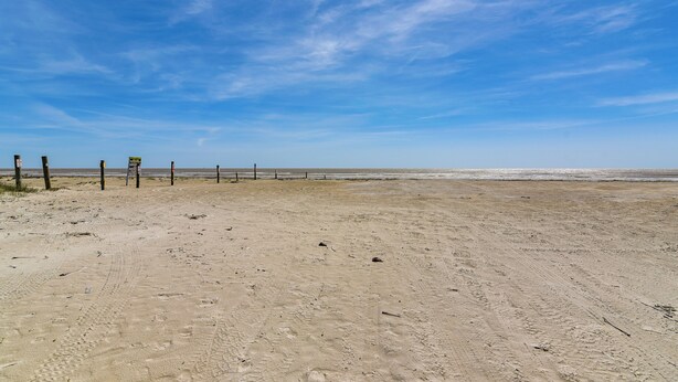 En sandstrand med ett staket och skyltar, under en klarblå himmel.