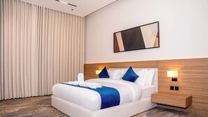 Une chambre d’hôtel moderne avec un grand lit, une tête de lit en bois, deux lampes de chevet et une grande fenêtre avec des rideaux.