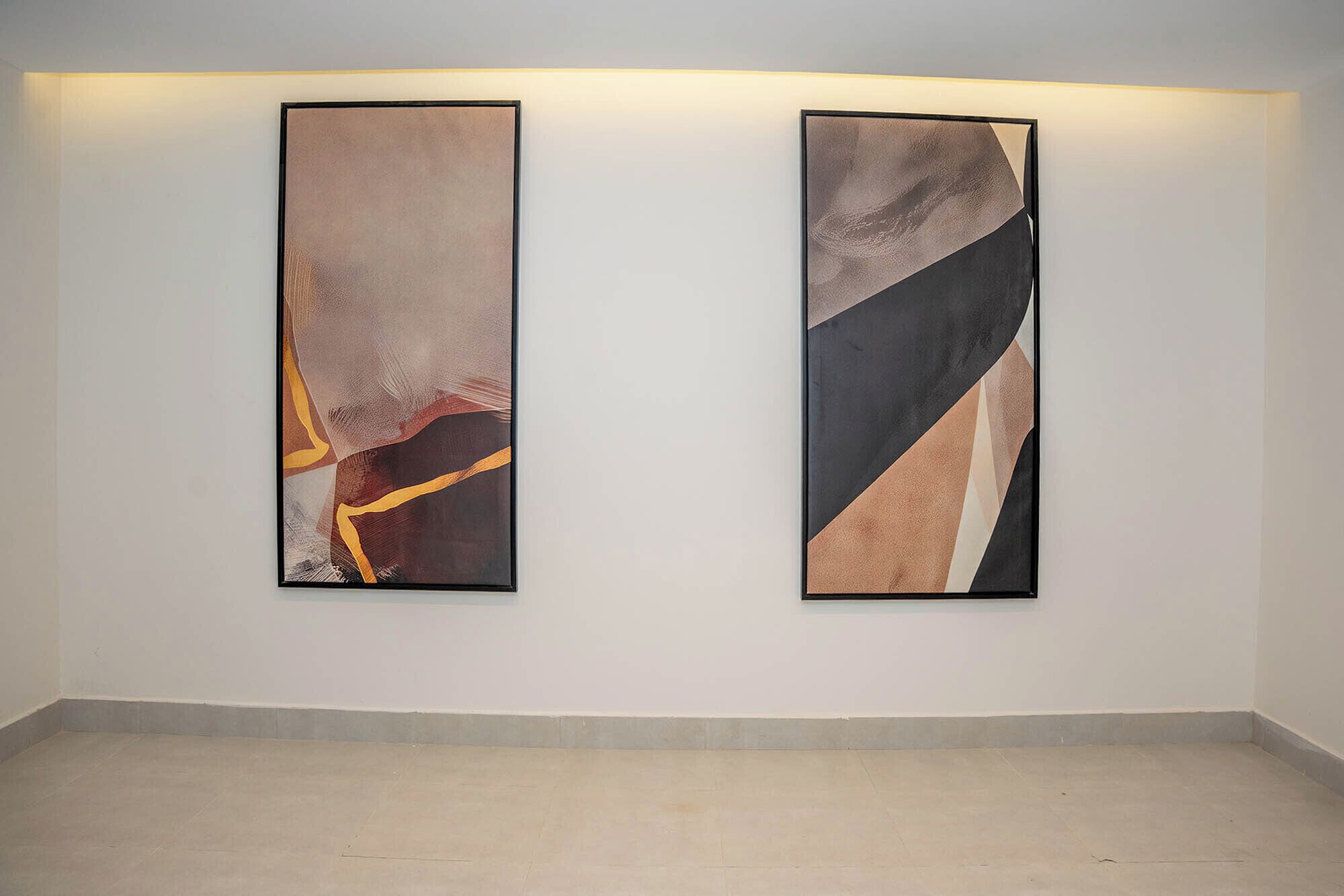 Two abstract paintings on a plain wall in a room with a tiled floor.