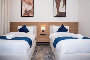 Camera d'albergo con due letti, un poggiatesta in legno, una lampada a parete e delle opere d'arte.