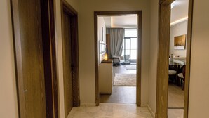 A hallway leading to a room with a bed, a desk, and a chair. - Alsawah - Skyline 3BR - Aeon Towers (6th of October City)