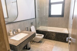 A modern bathroom with a marble sink, a toilet, and a bathtub. - Alsawah - Skyline 3BR - Aeon Towers (6th of October City)