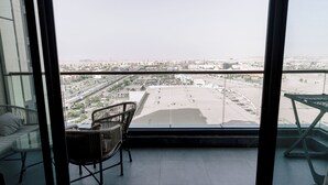 A balcony with a view of a cityscape, a wicker chair, and a glass table. - Alsawah - Skyline 3BR - Aeon Towers (6th of October City)