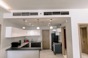 A modern kitchen with white cabinets, a black countertop, a built-in microwave, a stove, and a refrigerator. There are three pendant lights hanging from the ceiling. - Alsawah - Skyline 3BR - Aeon Towers (6th of October City)