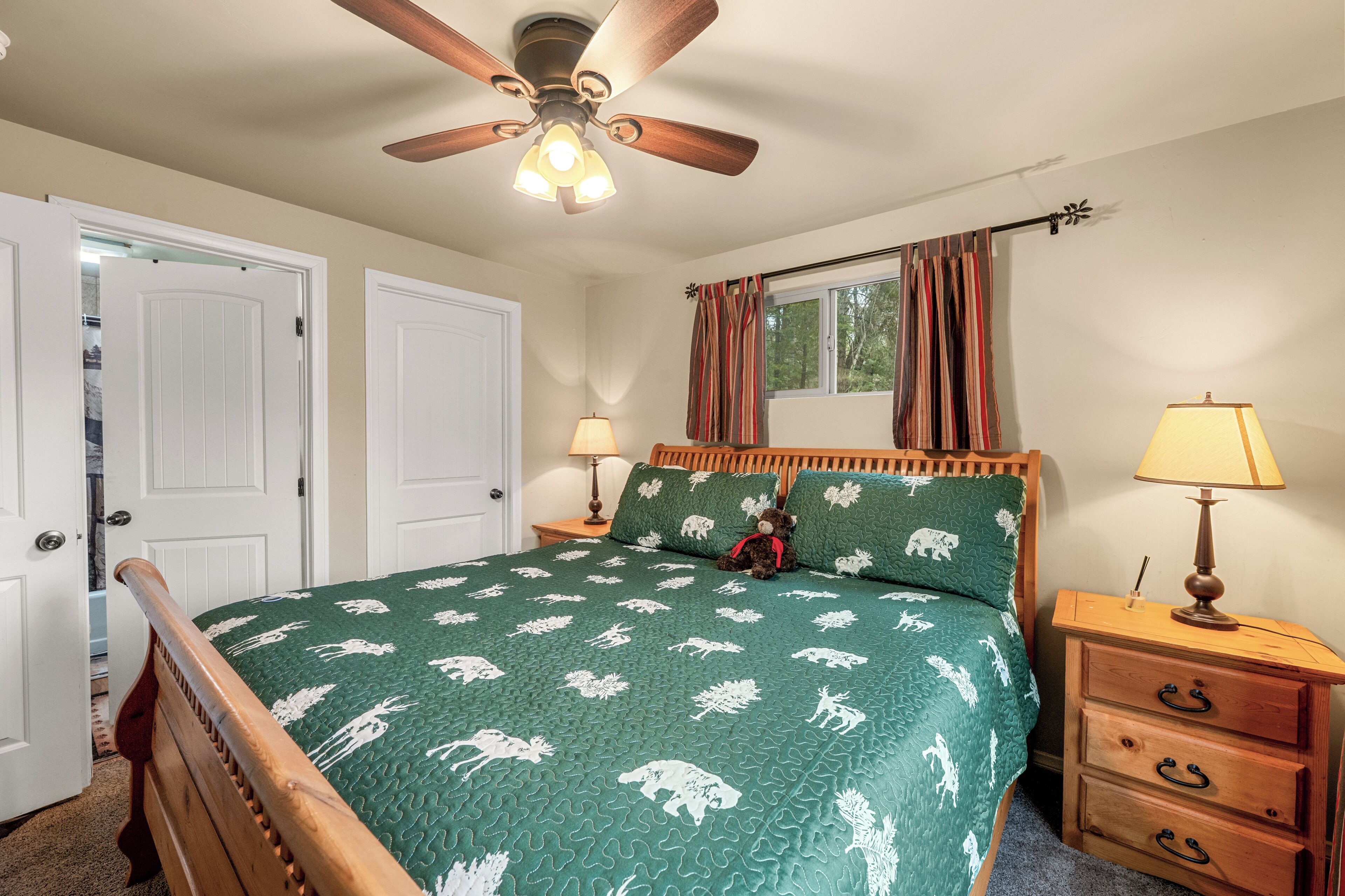 A bedroom with a bed, two bedside tables, a ceiling fan, and a window with curtains.