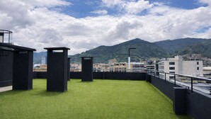 Una terrazza sul tetto con prato sintetico, pilastri neri e uno skyline con montagne sullo sfondo.