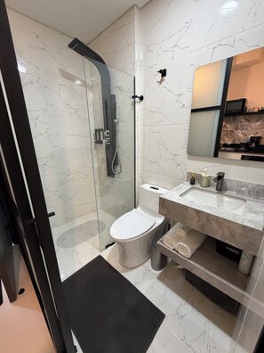 Ein modernes Badezimmer mit einer gläsernen Duschkabine, einer Toilette, einem Waschbecken mit Marmorplatte und einem Spiegel darüber.