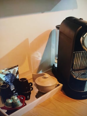 Keittiönurkkaus, jossa on kahvinkeitin, teekannu, kuppeja ja paketti kahvia.