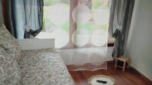 A room with a patterned sofa, a small wooden stool, and a window with curtains. - Walde Apartment w Warszawie (Warsaw)