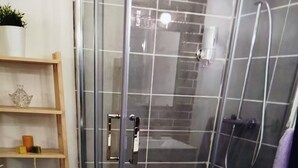 A glass-enclosed shower with a tiled wall, a wooden shelf with decorative items, and a white cabinet. - Walde Apartment w Warszawie (Warsaw)