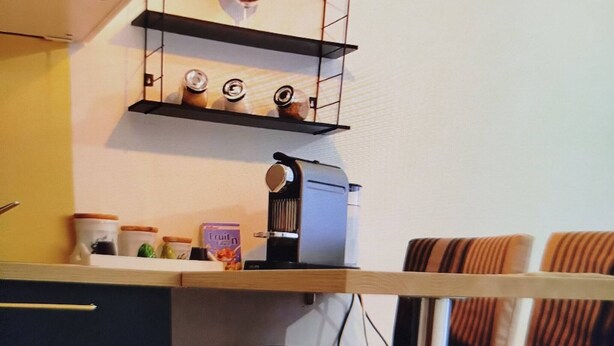 A kitchen with a coffee machine, shelves with jars, and a hanging light bulb. - Walde Apartment w Warszawie (Warsaw)