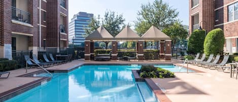 Une piscine avec des chaises longues, un kiosque et un bâtiment en briques en arrière-plan.