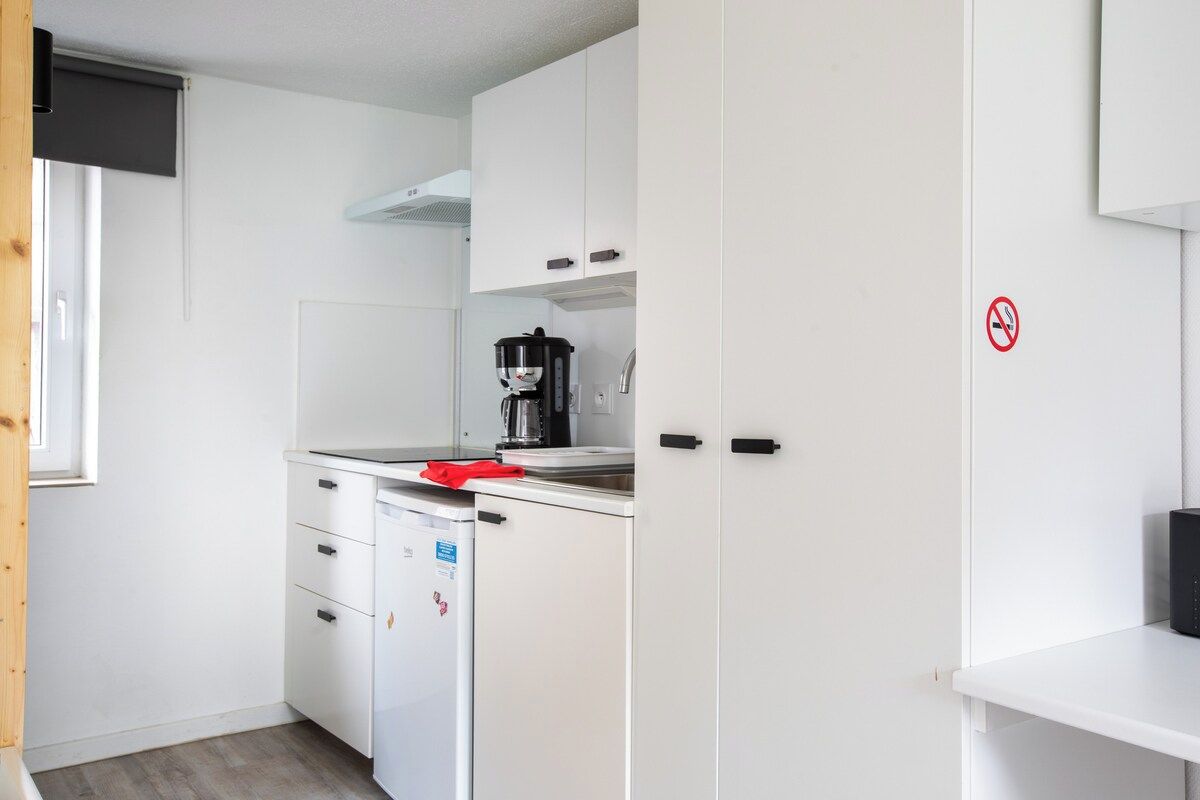 Una cocina compacta con armarios blancos, cafetera y refrigerador.