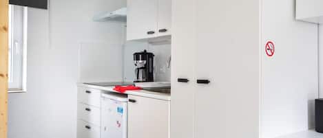 A compact kitchen with white cabinets, a coffee maker, and a refrigerator.