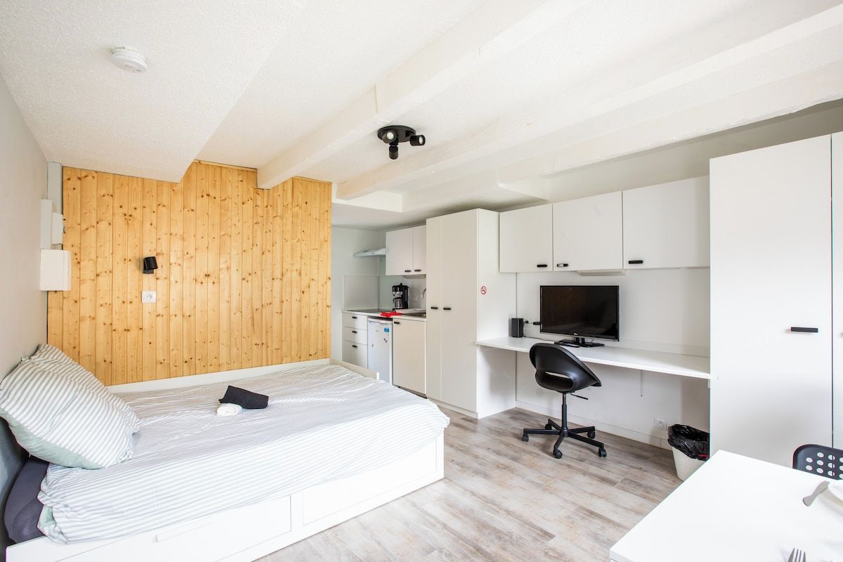 Una habitación funcional con cama, escritorio, televisión y kitchenette.
