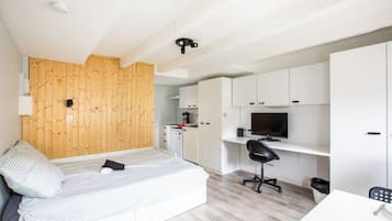 Una habitación funcional con cama, escritorio, televisión y kitchenette.