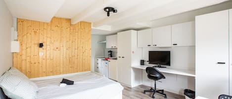 Une chambre de taille modeste comprenant un lit, un bureau, une télévision et un coin cuisine.